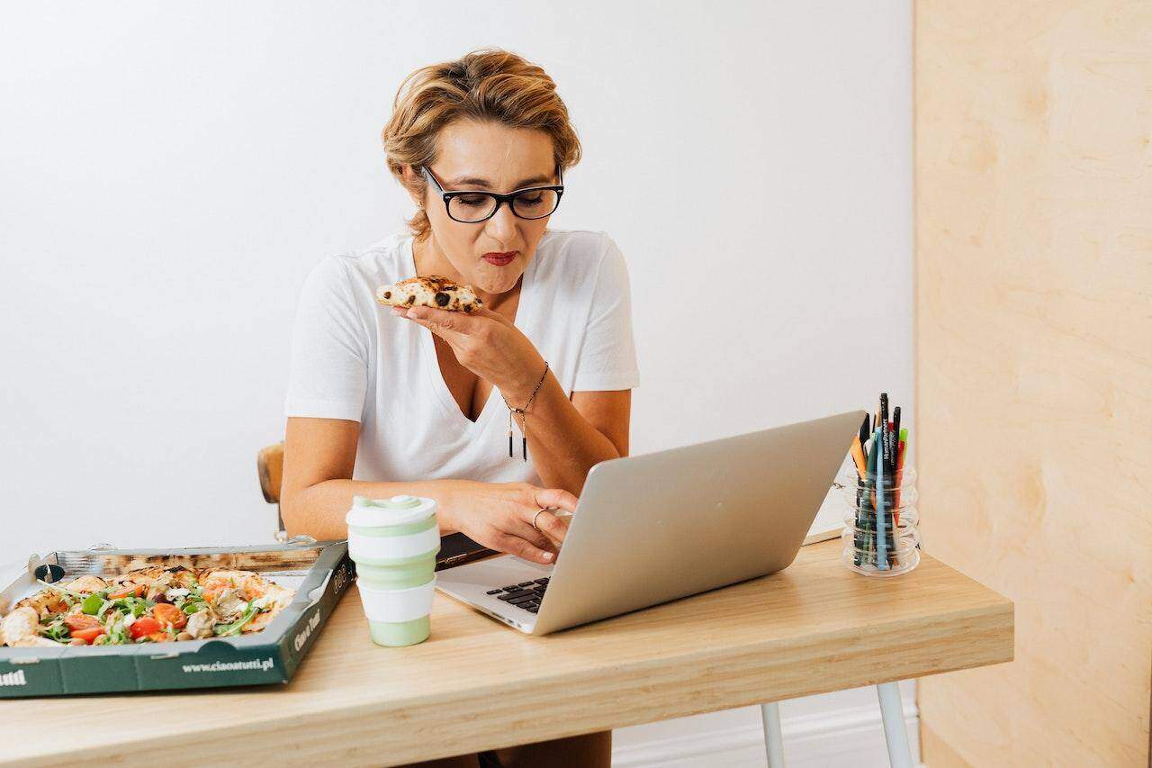 kobieta jedząca oraz przeglądająca internet z laptopem